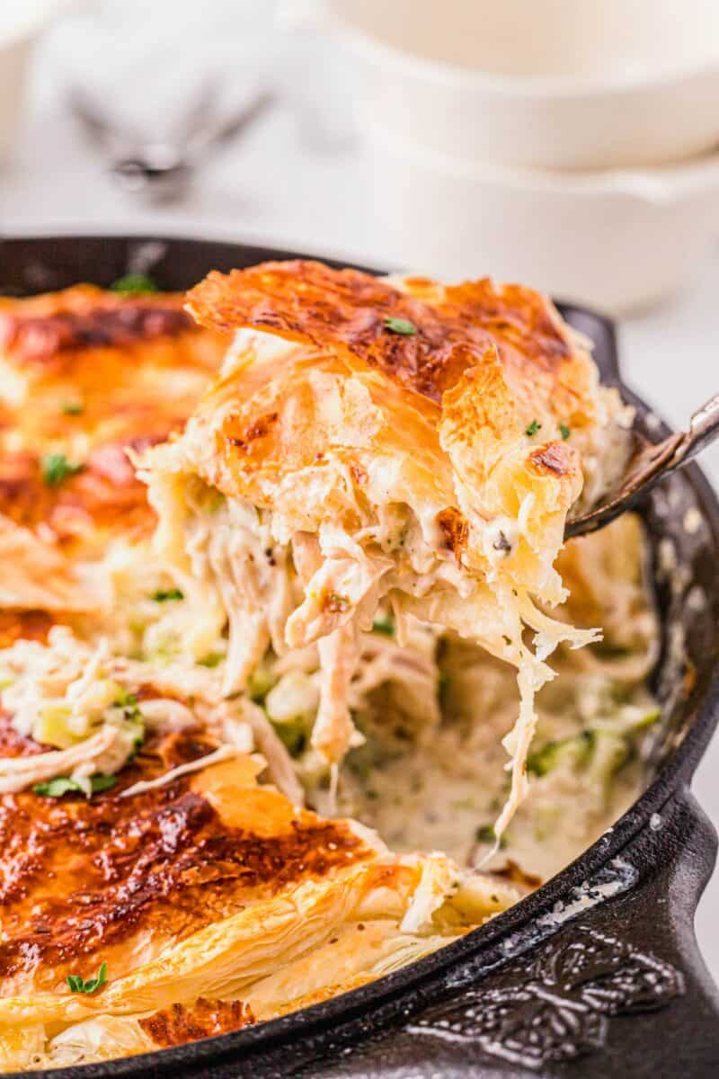 A serving of chicken alfredo pot pie is being lifted from the black cast iron skillet.