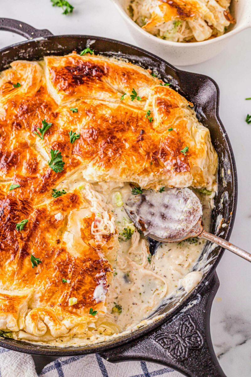 A large serving spoon is placed in a skillet with alfredo pot pie.