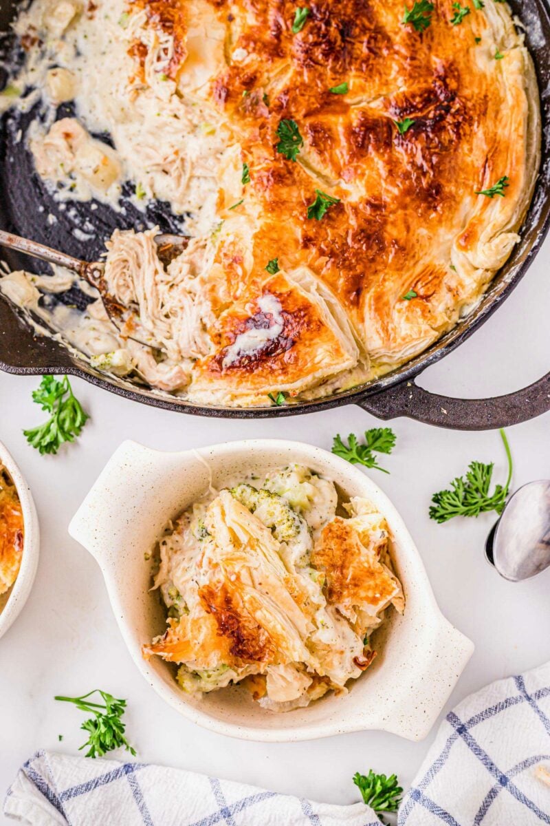 A serving of pot pie is placed in a white bowl next to a large skillet.