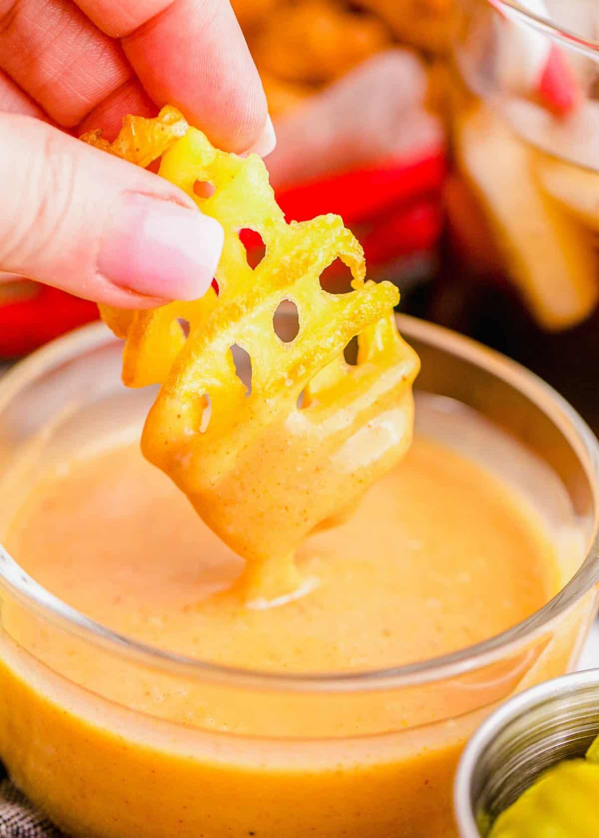 Hand dipping waffle fry into Chick-Fil-A sauce