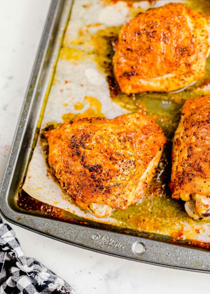 Several baked chicken thighs are on a sheet of parchment paper on a sheet pan.