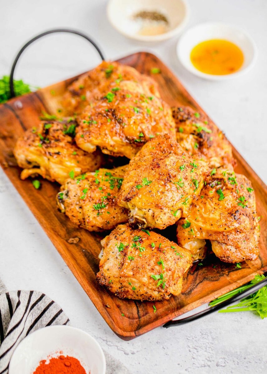 A wooden serving platter is topped with multiple baked chicken thighs. 