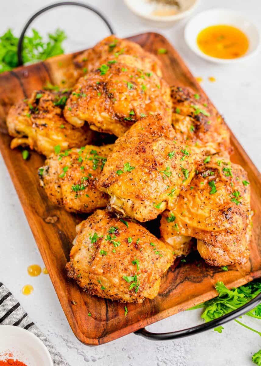 A large serving of chicken thighs is presented on a large wooden serving platter.