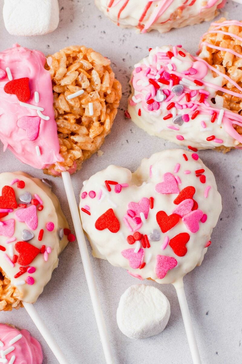 Heart shaped sprinkles are scattered across the top of a white chocolate covered rice krispies heart.