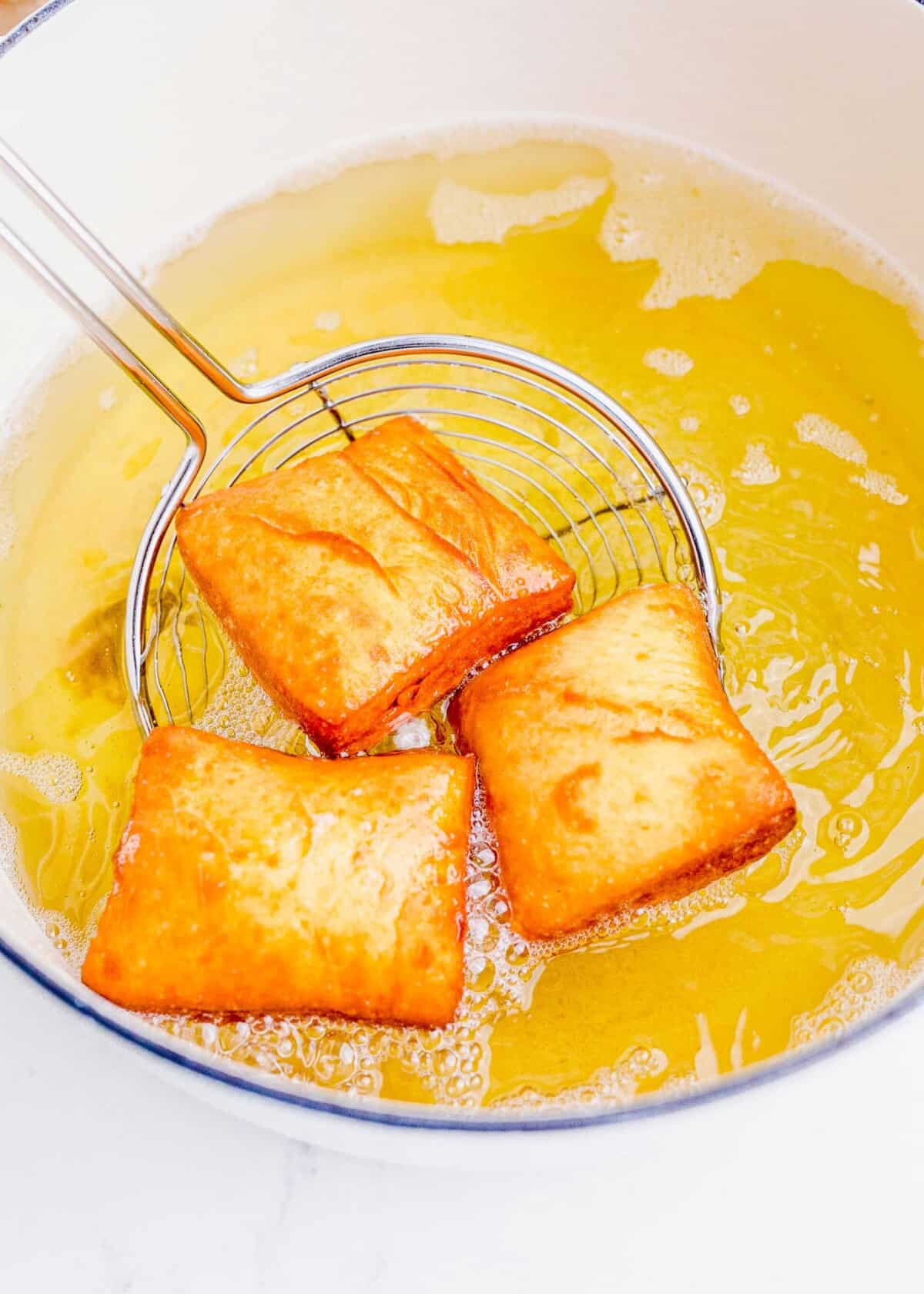 Three beignets are being fried in a large pot full of yellow vegetable oil.