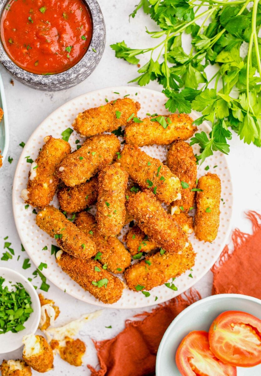 A round white plate filled with mozzarella stick is presented on a crowded white countertop.