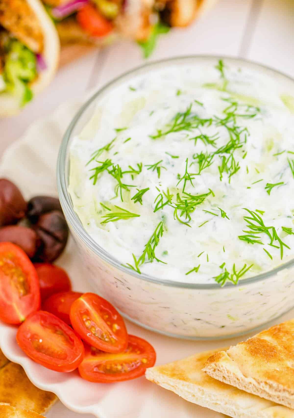 Tzatziki dip in glass bowl with olives, grape tomatoes, and pita