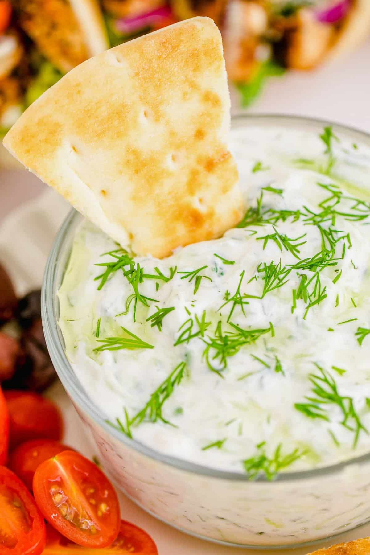 Pita chip in bowl of tzatziki dip garnished with dill and olive oil