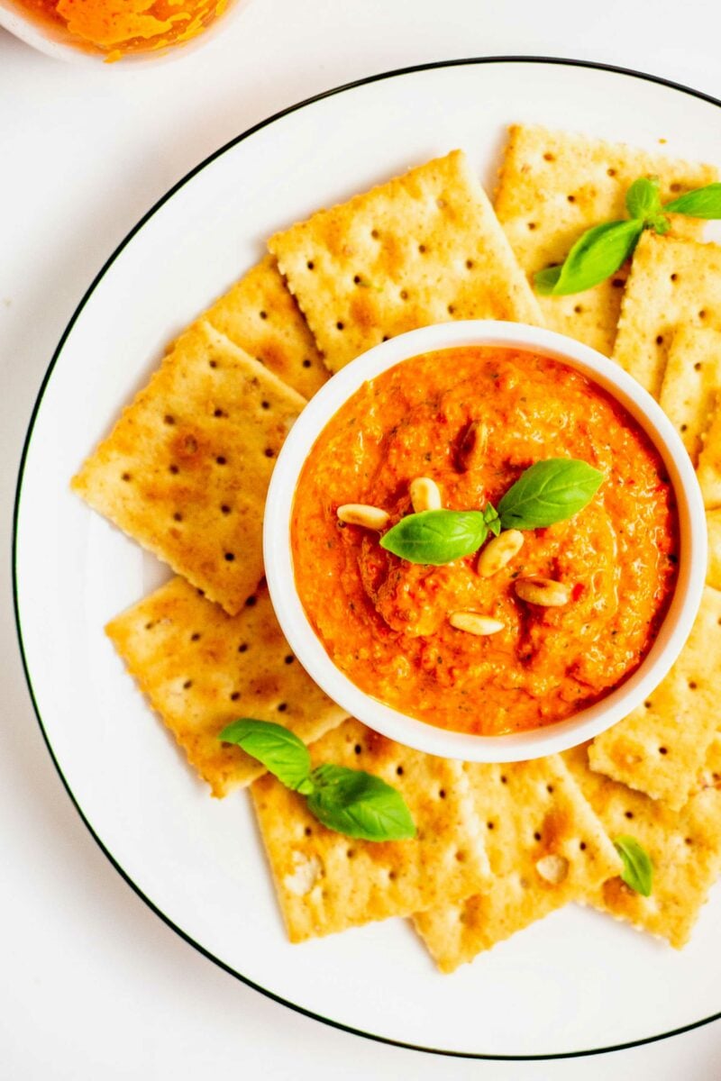 overhead shot of roasted red pepper pesto in a small white bowl surrounded by saltine crackers