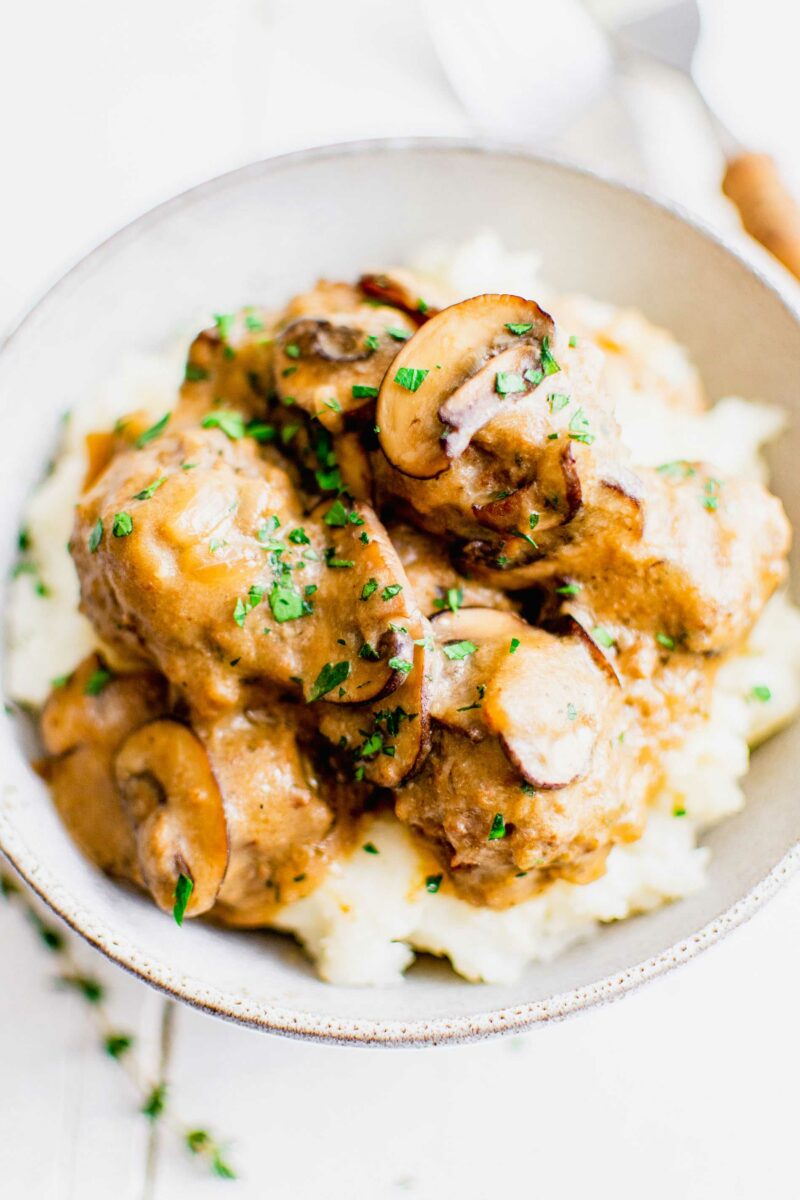 A white bowl is filled with mashed potatoes, gravy, and meatballs. 