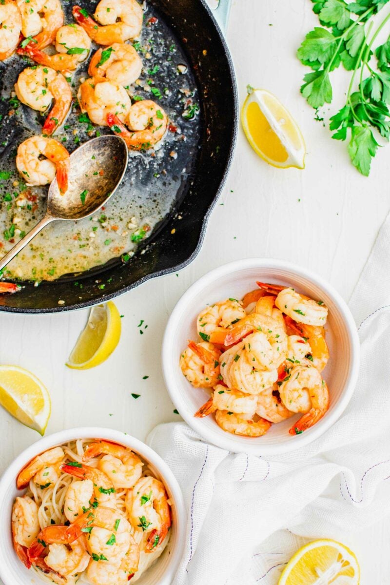 Two white bowls of cooked shrimp are placed next to a black skillet.