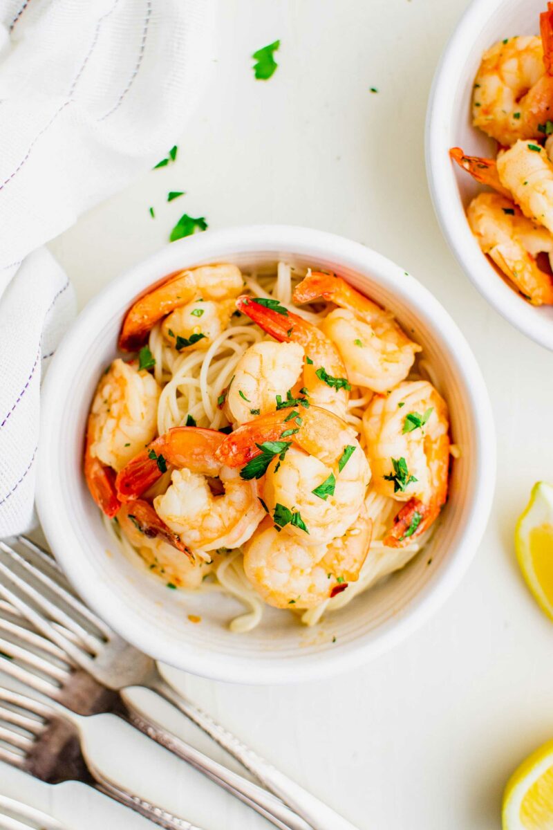 A white bowl is filled with pasta, shrimp, and topped with fresh parlsey.