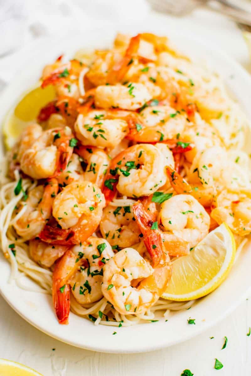 A plate of shrimp scampi is topped with fresh herbs and a lemon wedge.