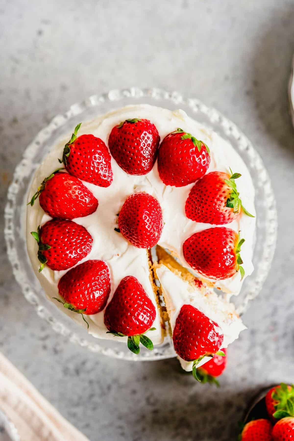 Overhead view of strawberry sponge cake, decorated with strawberries and one slice being removed