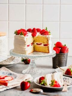 Strawberry sponge cake on cake stand with slices removed to show inside
