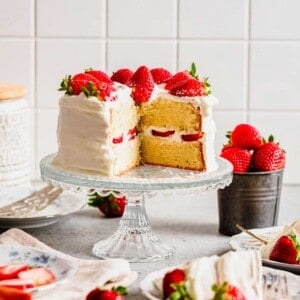 Strawberry sponge cake on cake stand with slices removed to show inside