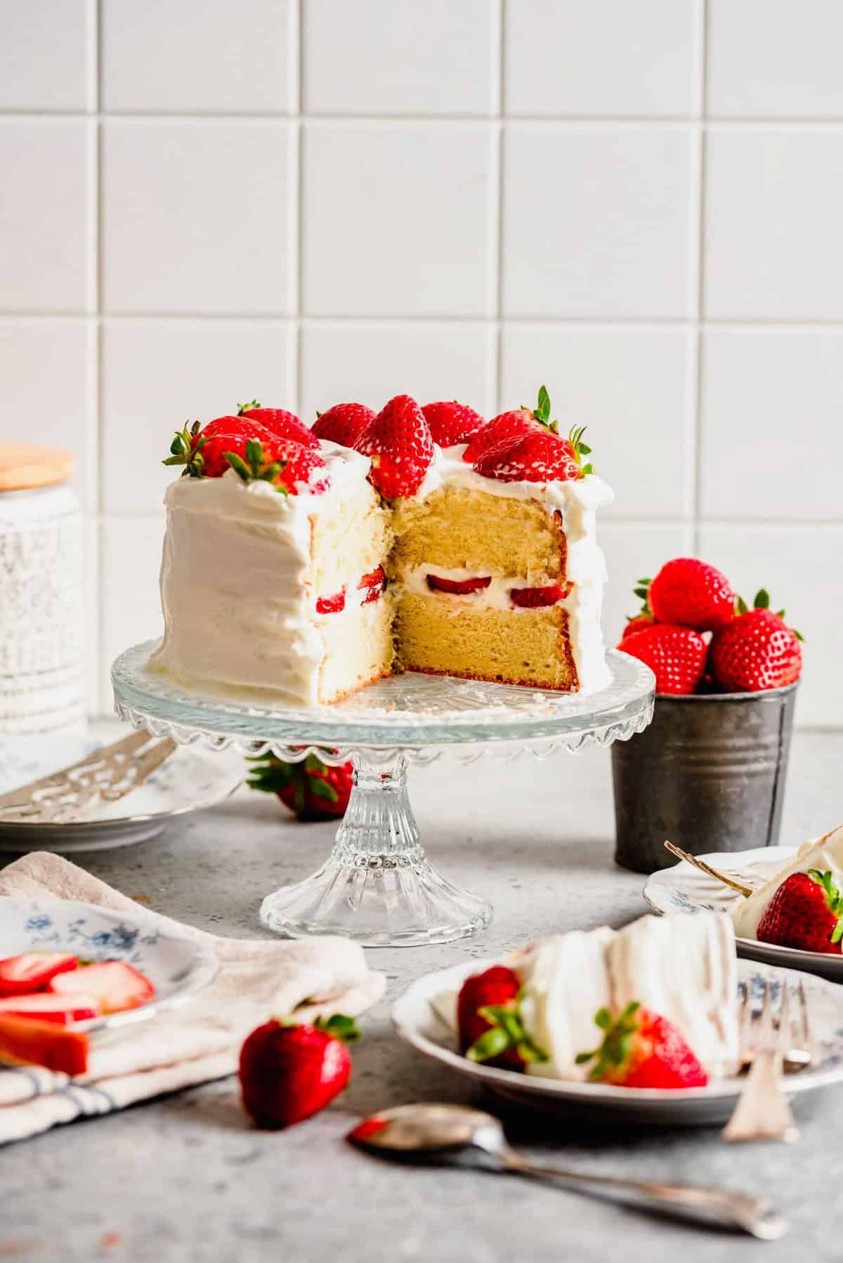Strawberry sponge cake on cake stand with slices removed to show inside