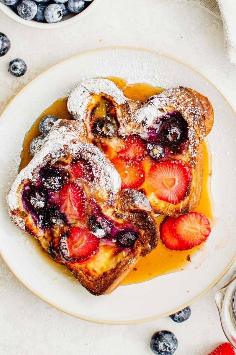 Maple syrup has been generously poured over two slices of cooked custard yogurt toast on a white plate.