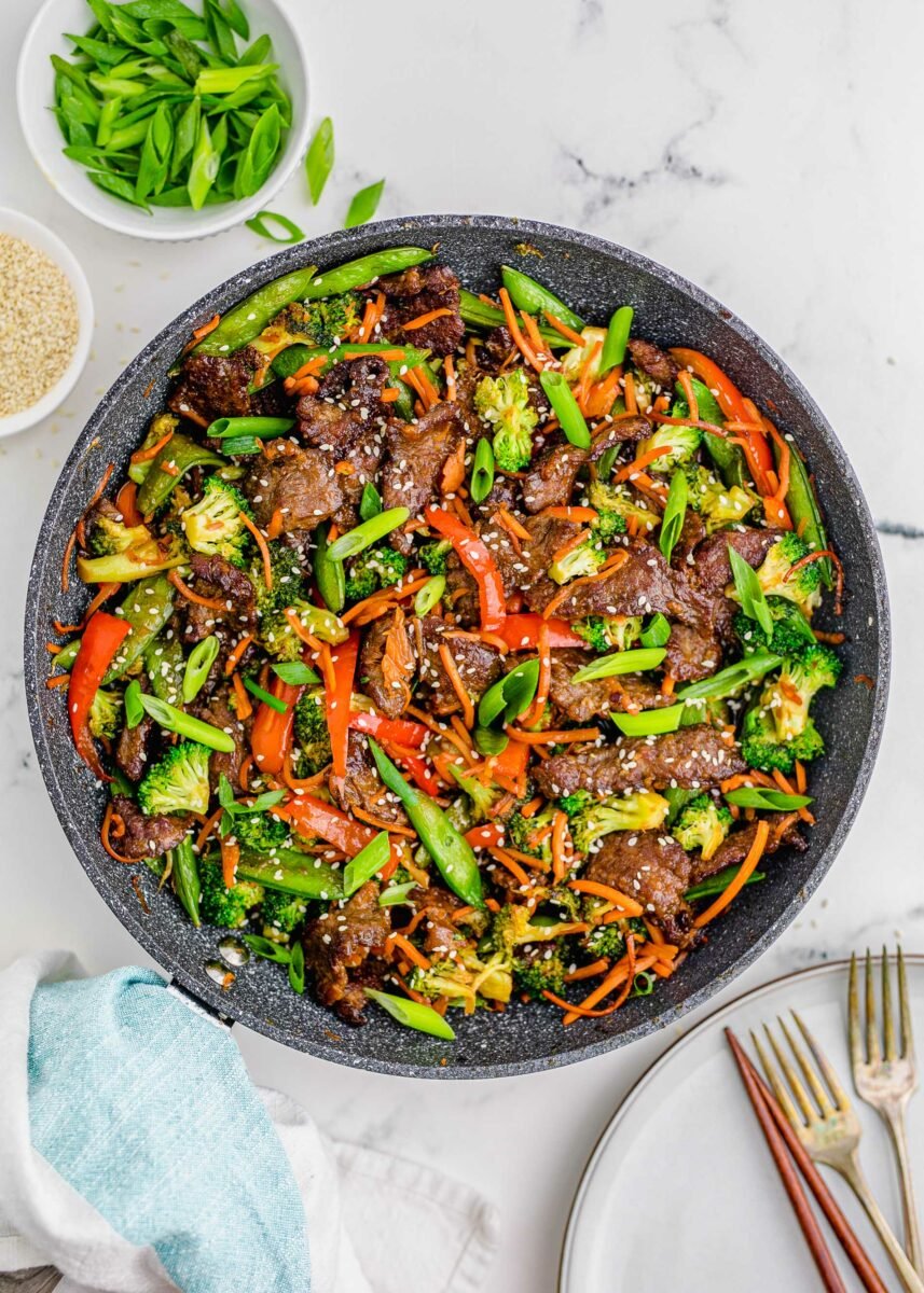 Steak and veggies have been cooked together in a skillet and garnished with sesame seeds.  