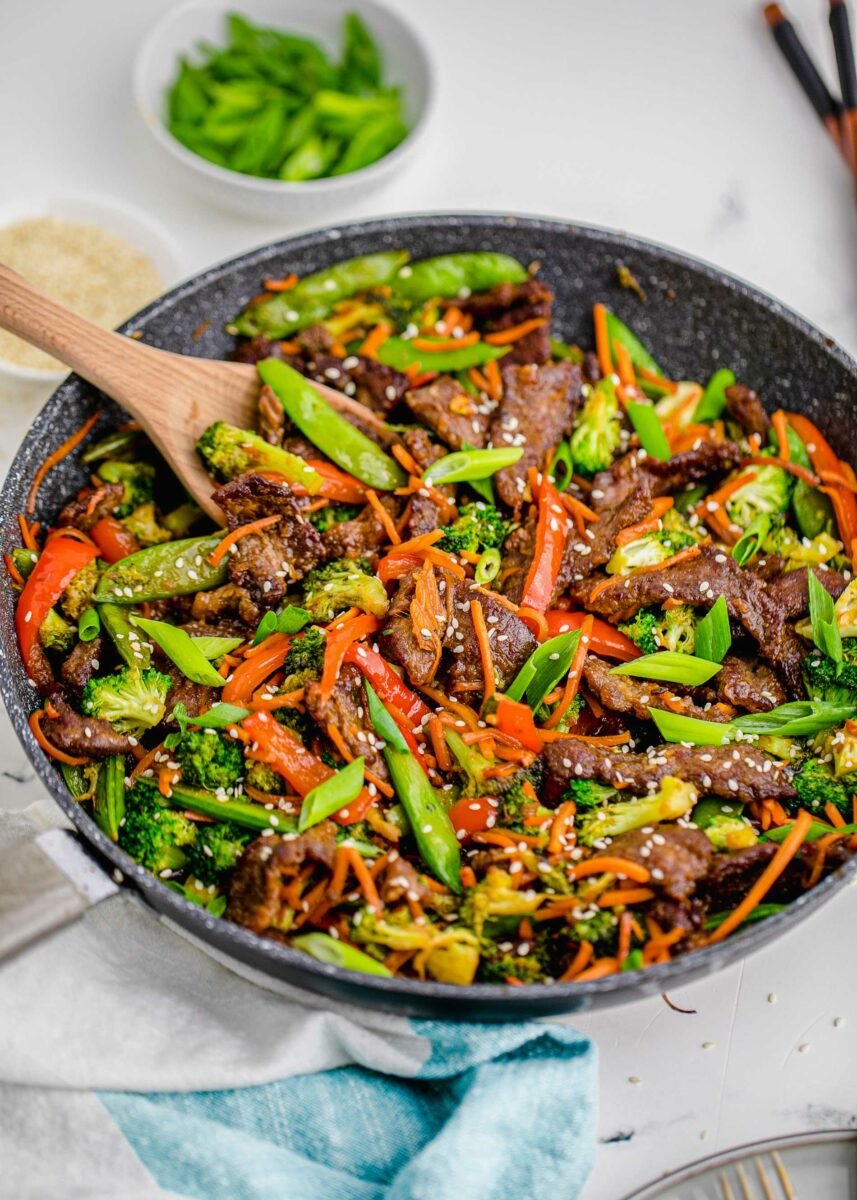 A large skillet is filled with steak, veggies, and sesame seeds. 