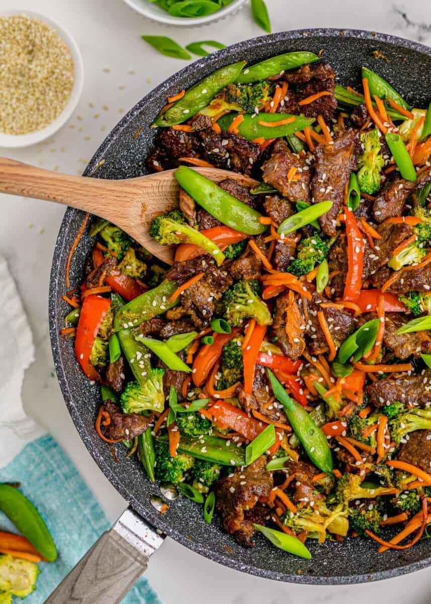A wooden spoon is placed in a skillet full of beef stir fry.