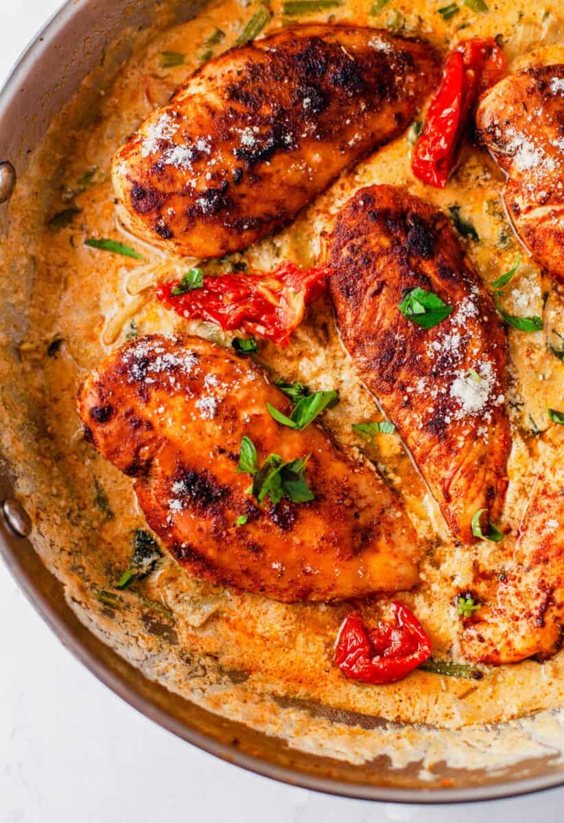 Cooked chicken breasts are placed in a pan filled with creamy orange sauce.