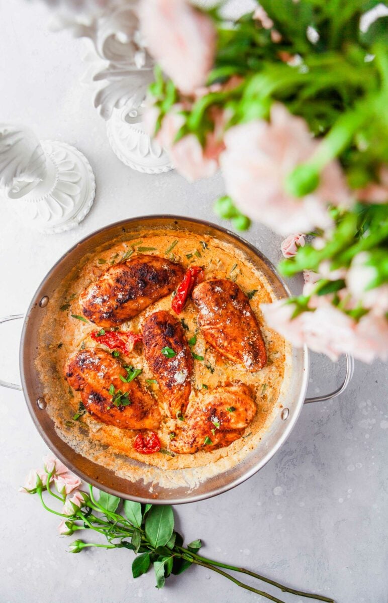 Five cooked chicken breasts are placed in a pan with sauce and fresh parsley. 