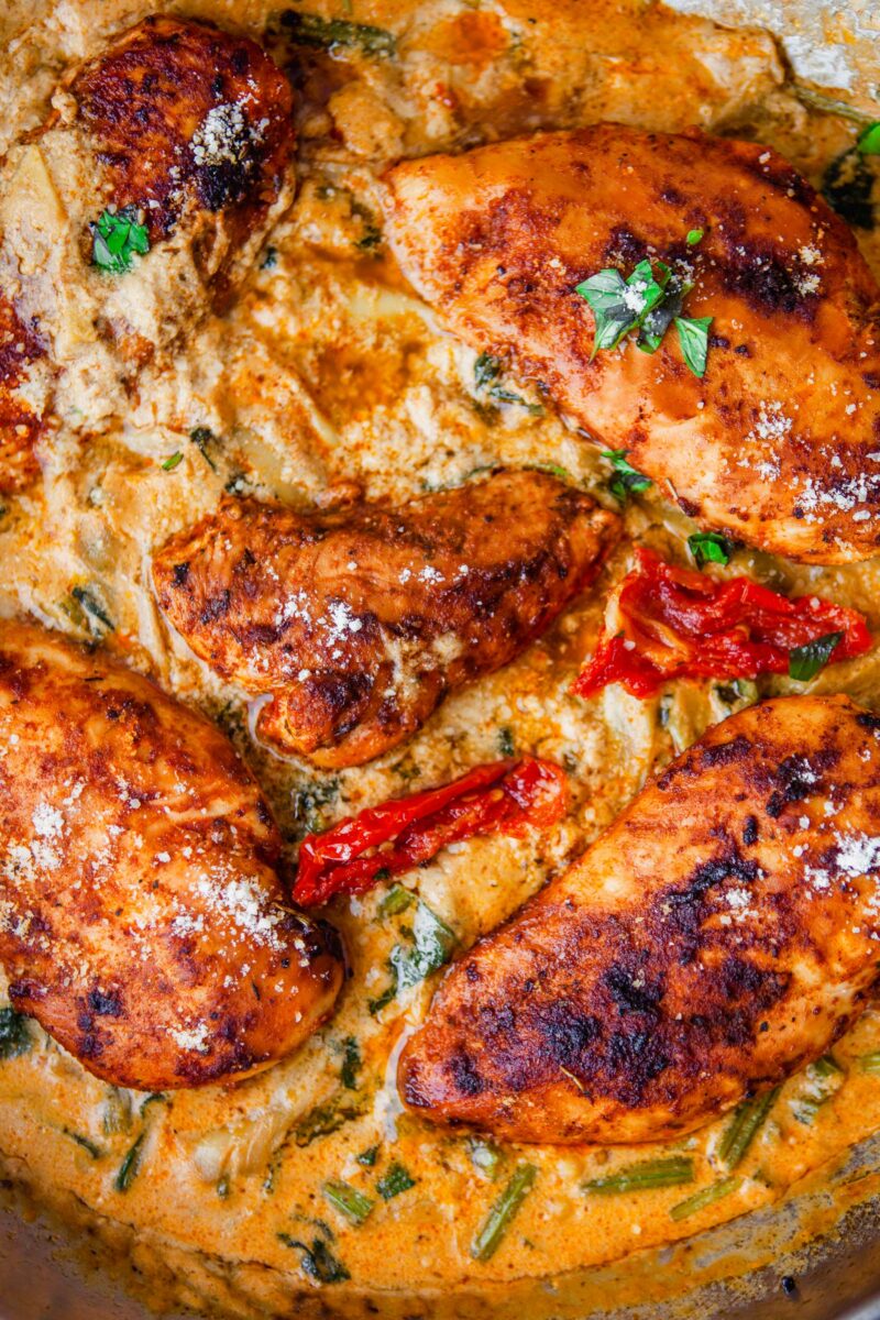 Sun-dried tomatoes and fresh herbs are on top of cooked, sauce coated chicken. 