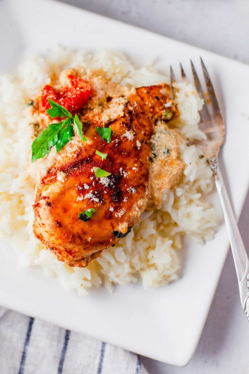 Chicken is served on a pile of white rice on a square white plate.