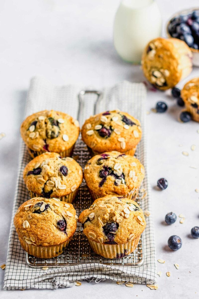 Half a dozen baked muffins are placed on a wire cooling rack above a checkerboard tea towel.