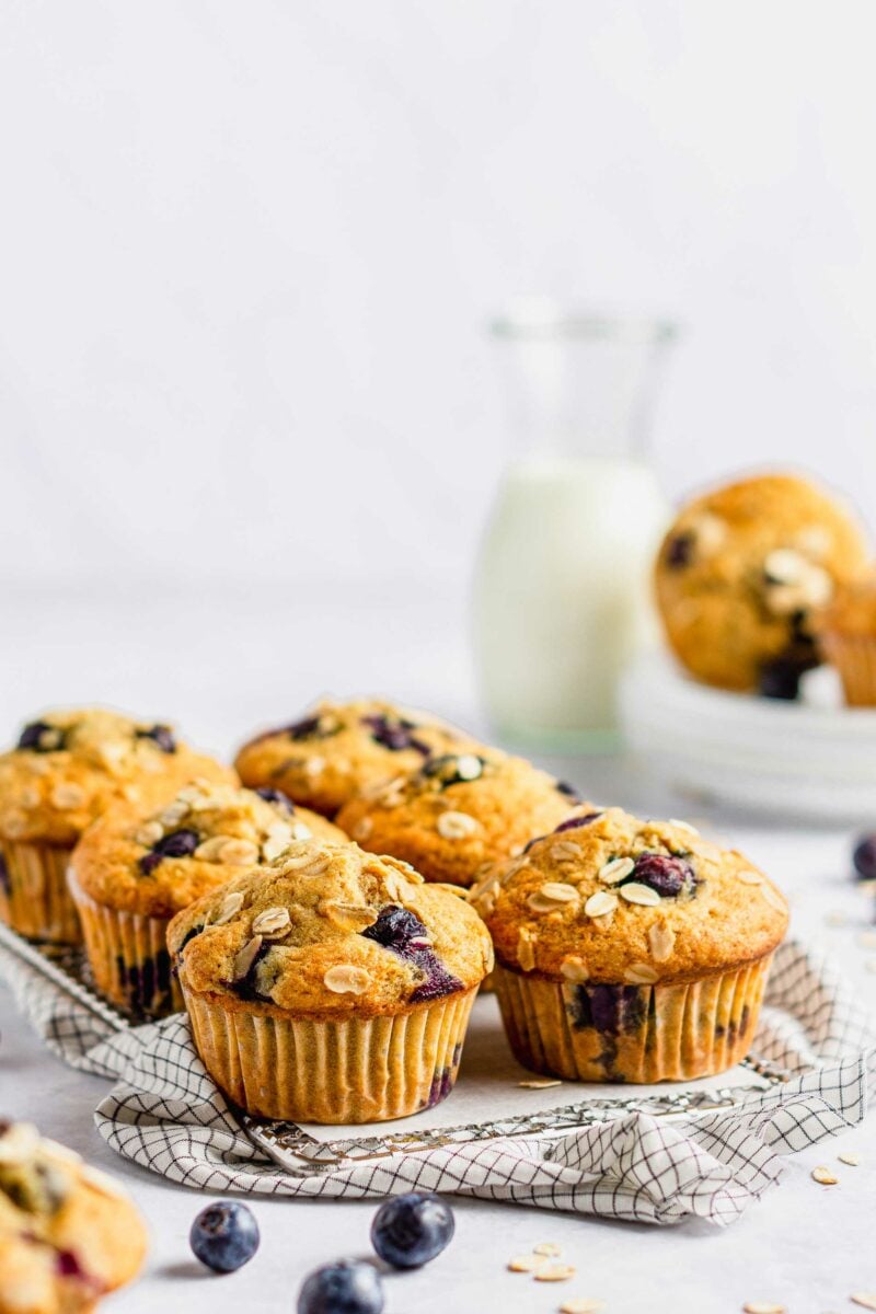 A few blueberries are scattered near the half dozen muffins on a countertop. 