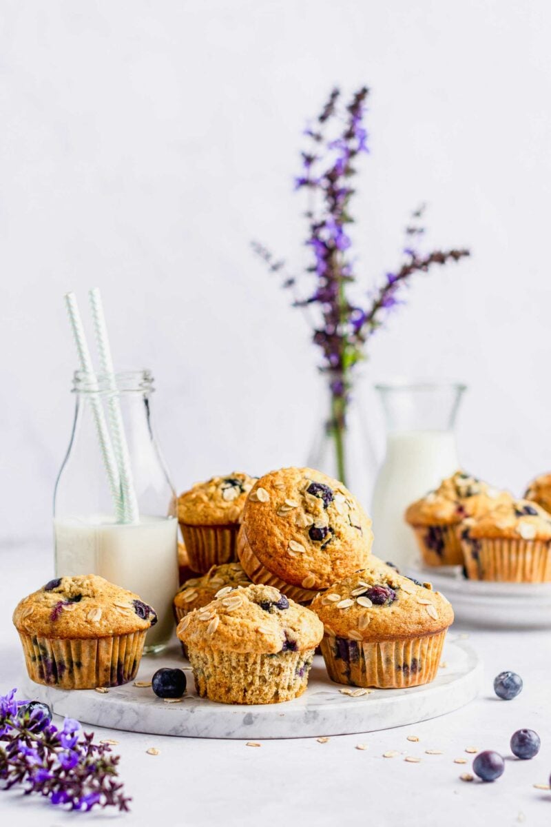 Lavender sprigs and a glass jar of milk are placed next to muffins on a marble serving platter.