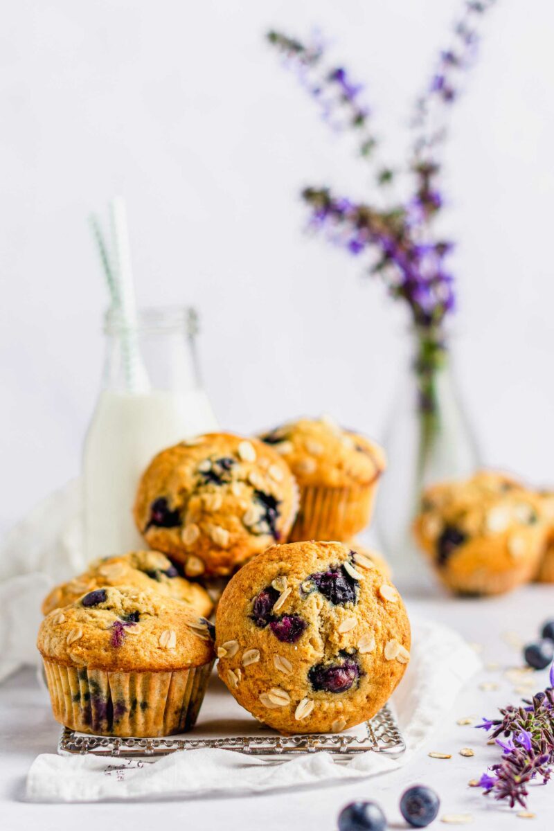A batch of oatmeal blueberry muffins are placed on a white countertop next to blueberries and lavender. 
