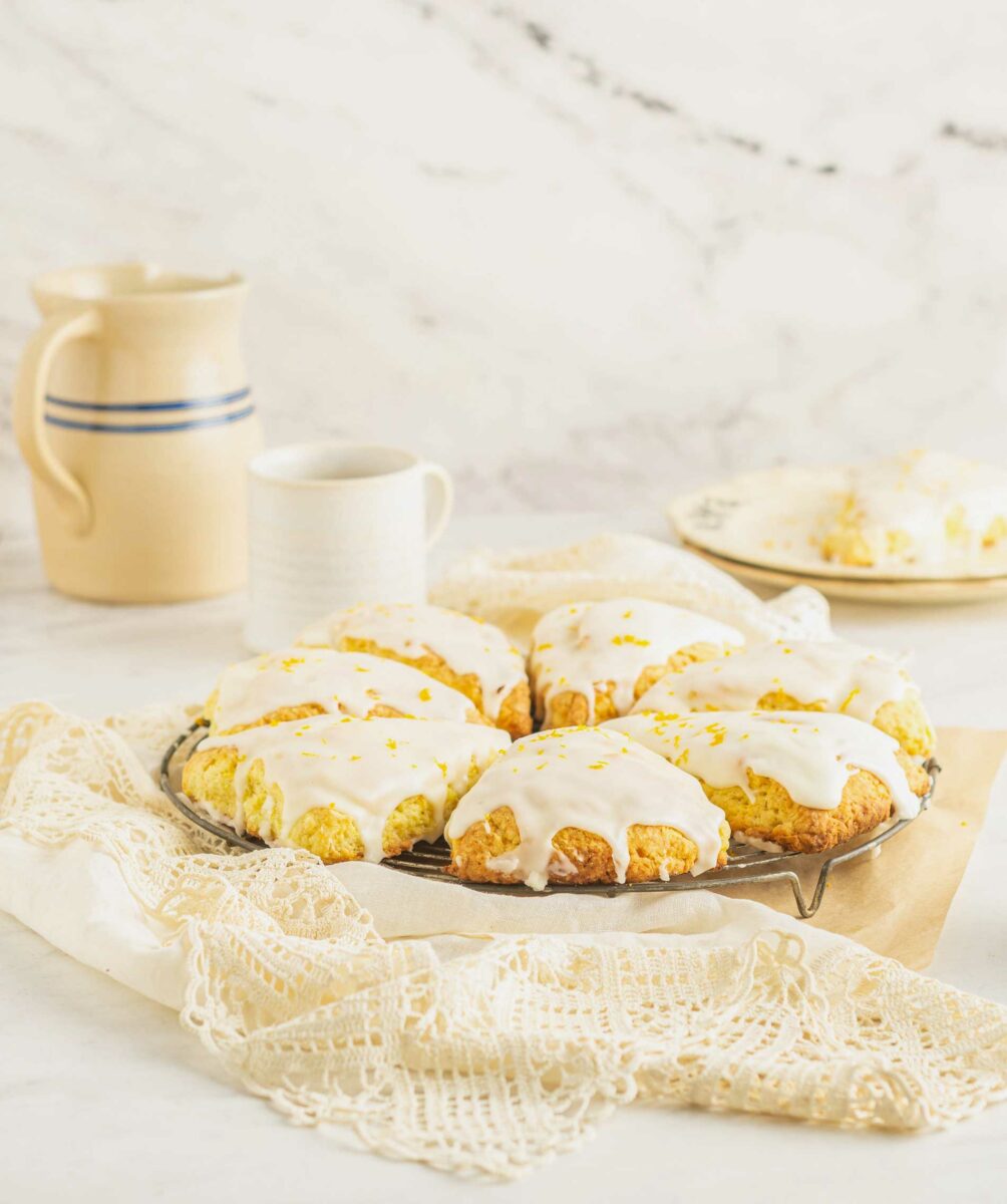 A batch of homemade scones is presented on a cooling rack on top of a white lace tablecloth. 
