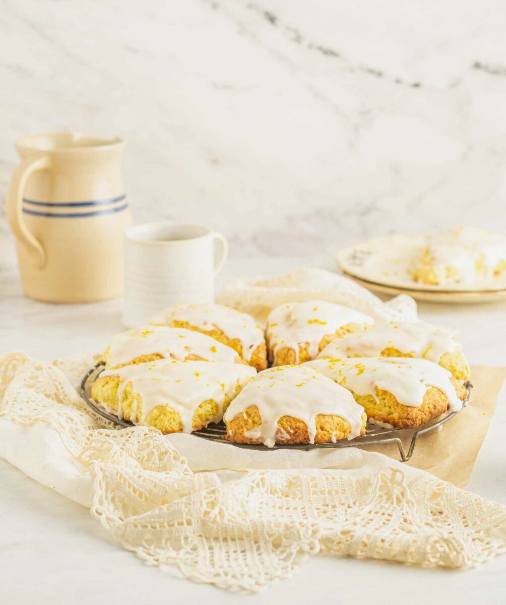 A batch of homemade scones is presented on a cooling rack on top of a white lace tablecloth.