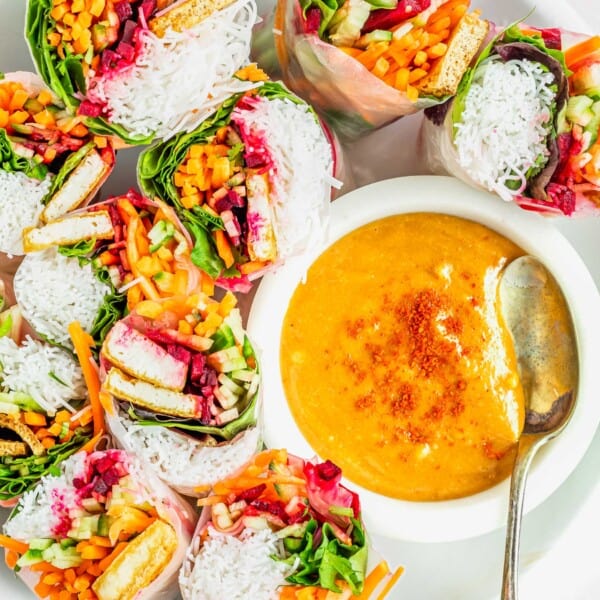 Overhead view of summer rolls arranged around a bowl of spicy peanut dipping sauce on a white plate.