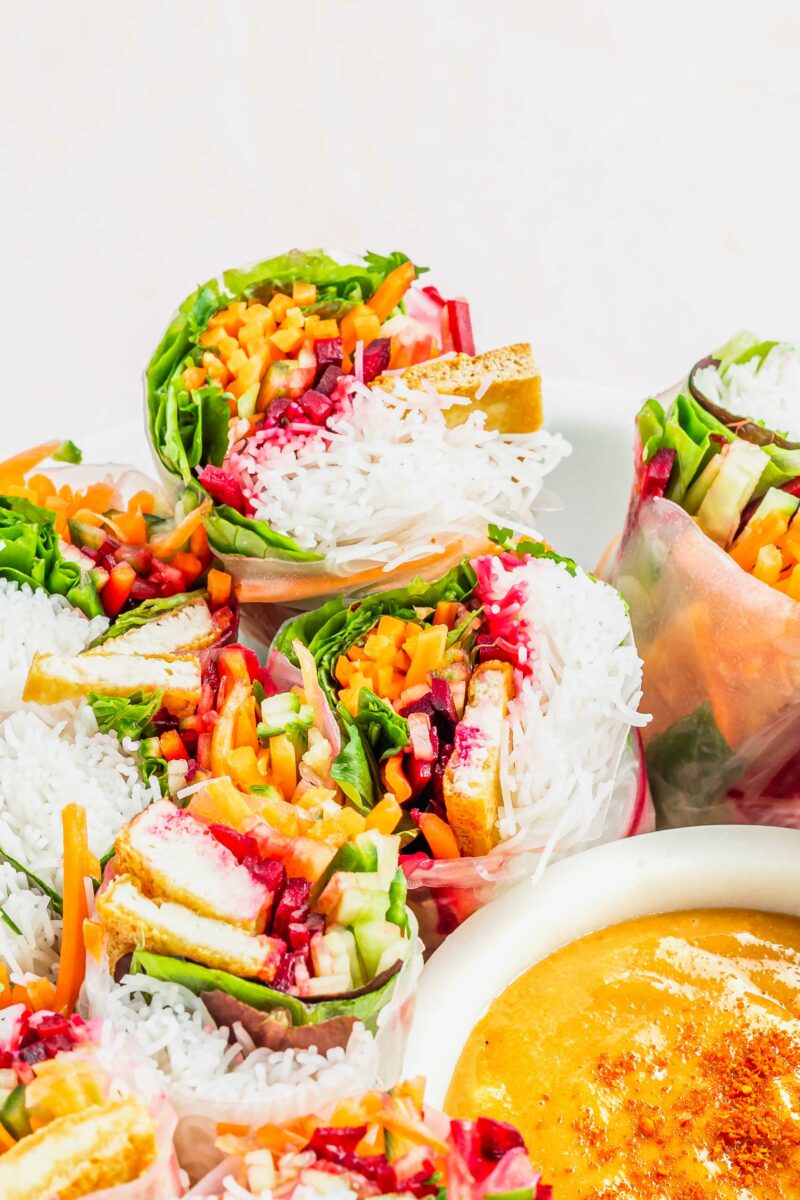 A platter of halved summer rolls is placed next to a small bowl of satay dipping sauce. 