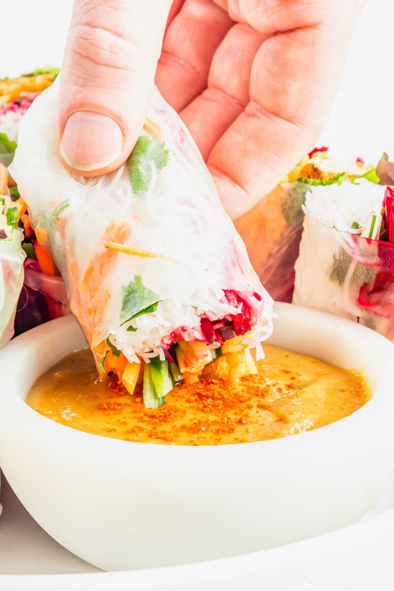 A halved summer roll is being dipped into peanut sauce. 