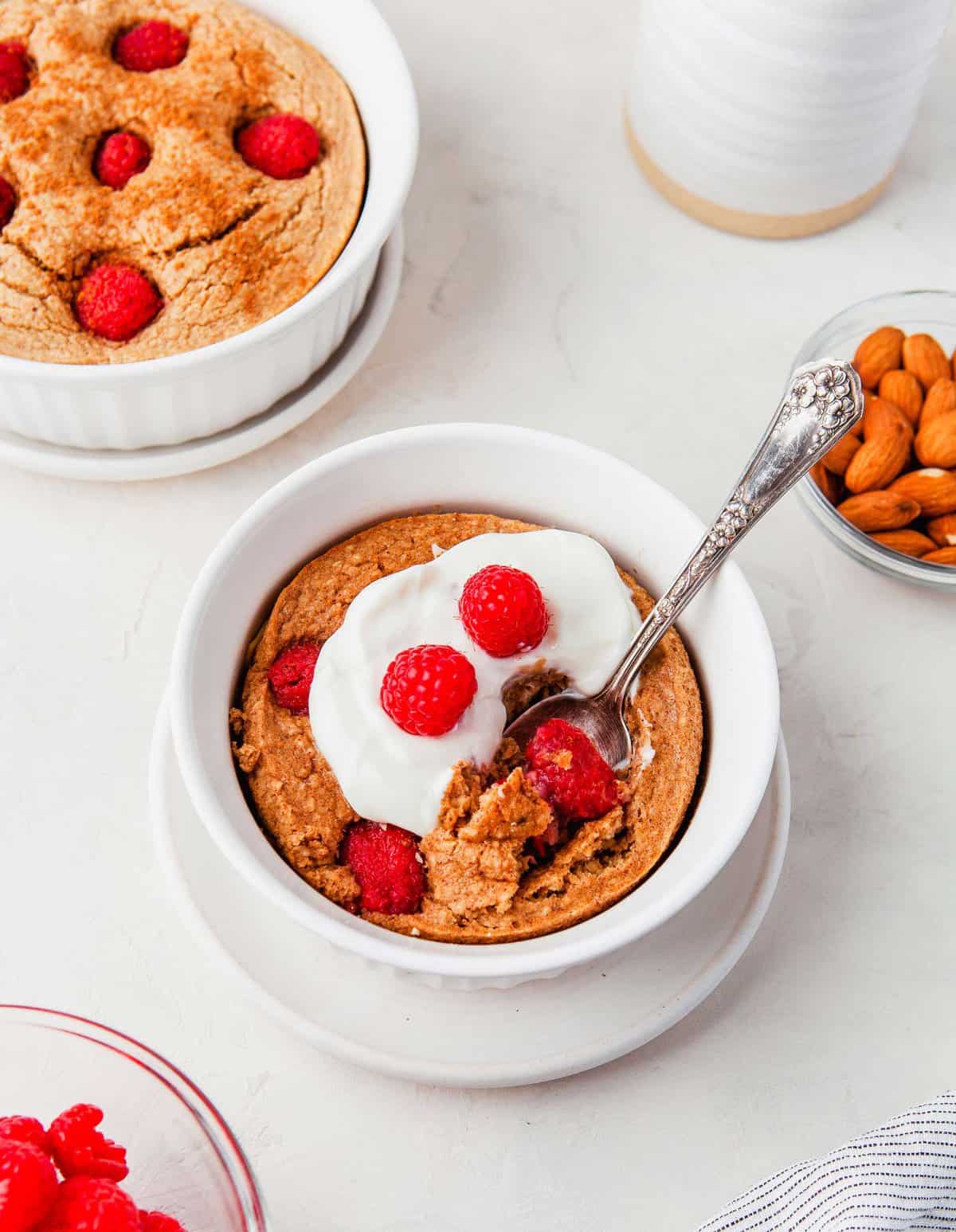Raspberry baked oatmeal in white bowl with spoon, garnished with yogurt and berries