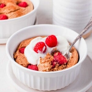 Raspberry baked oatmeal topped with yogurt and raspberries, in white bowl with spoon
