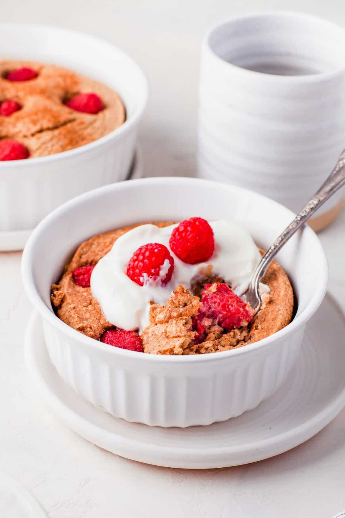 Raspberry baked oatmeal topped with yogurt and raspberries, in white bowl with spoon