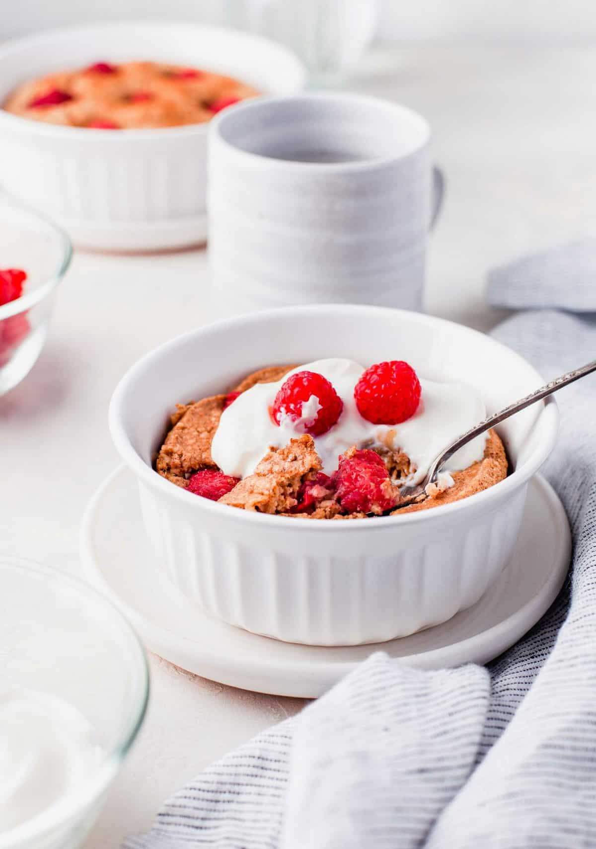 Raspberry baked oatmeal in white bowl with spoon, topped with yogurt and raspberries