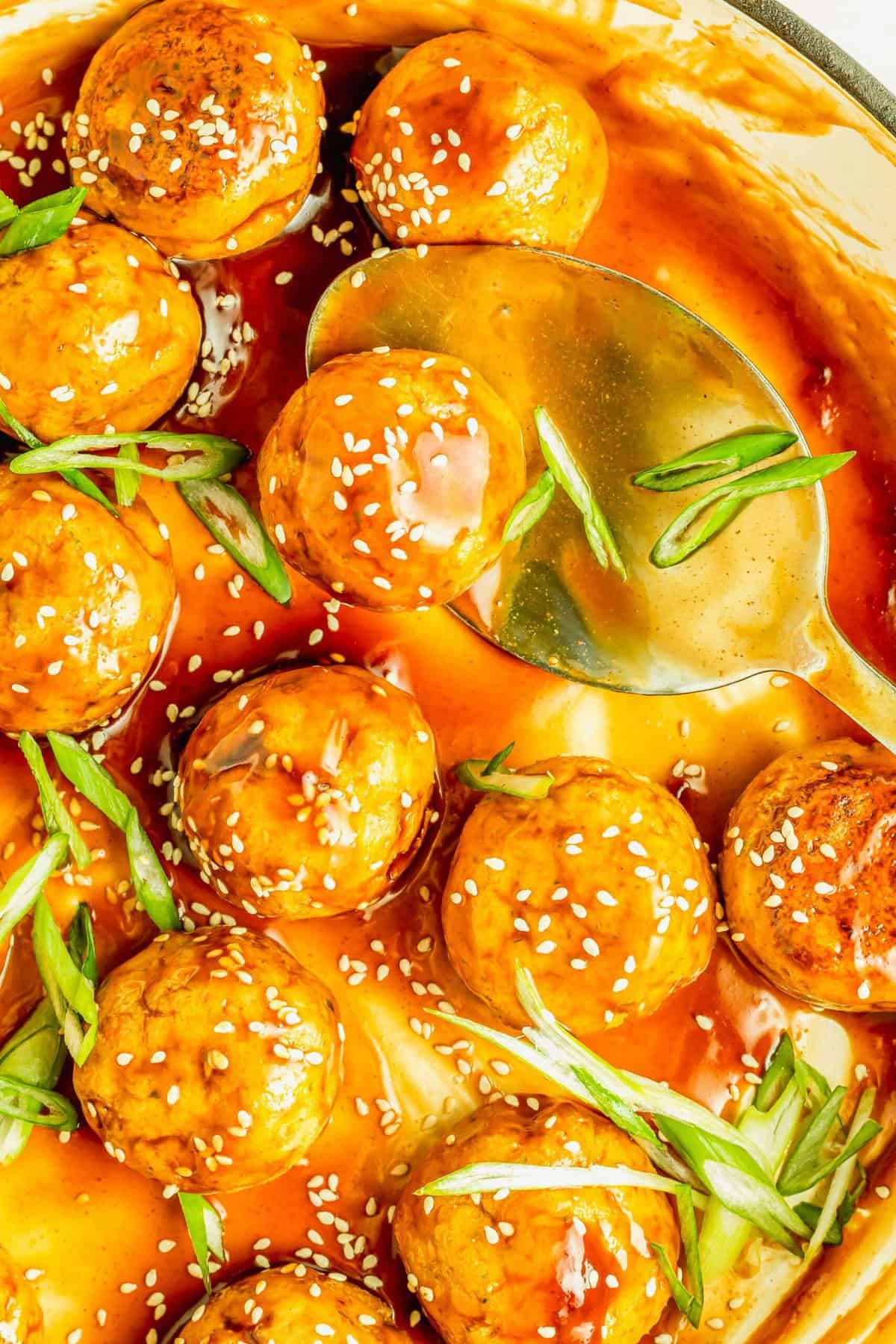 Overhead view of teriyaki-coated tofu meatballs in skillet with large spoon