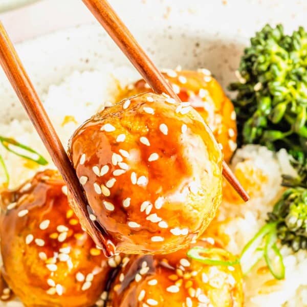 Chopsticks picking up teriyaki tofu meatball with sesame seeds