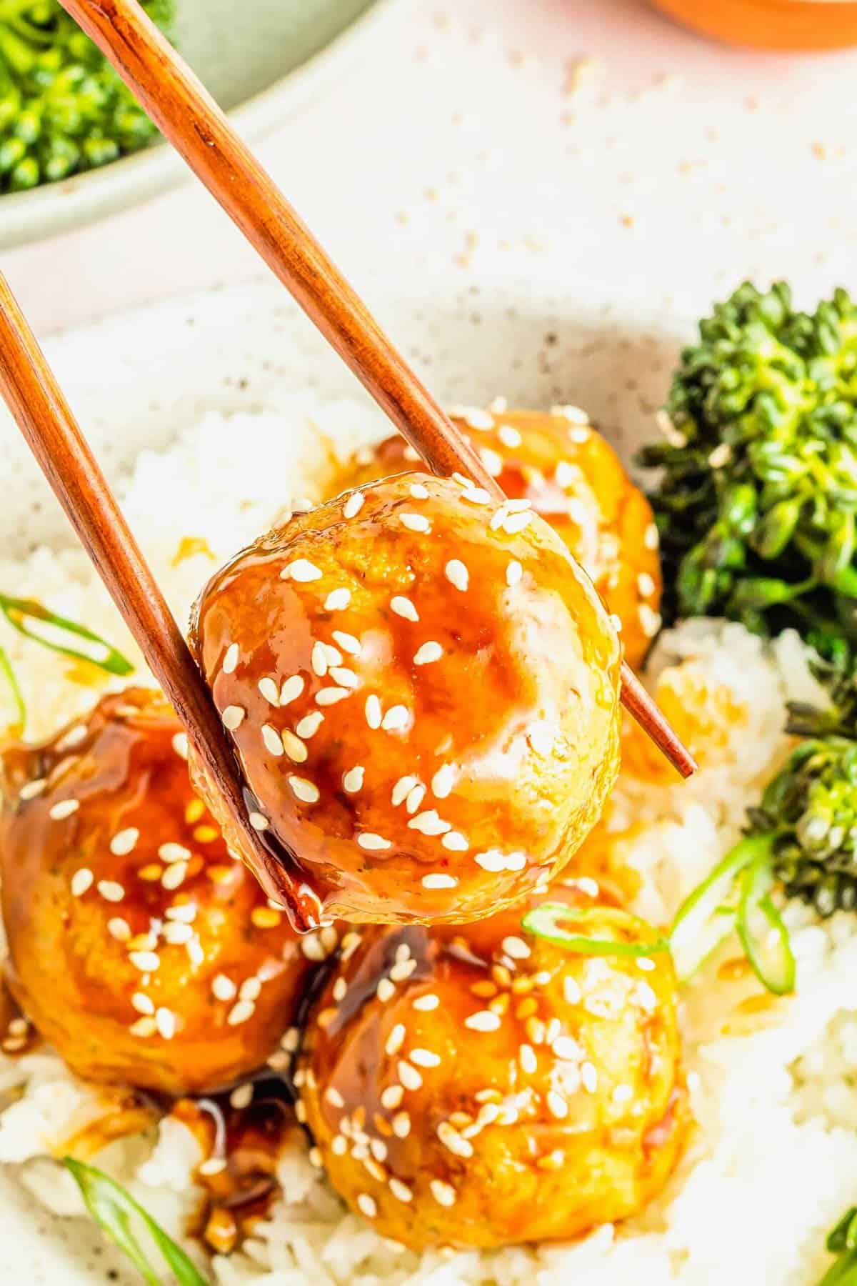 Chopsticks picking up teriyaki tofu meatball with sesame seeds