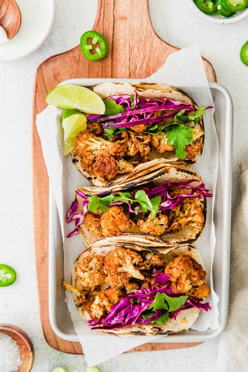 Three cauliflower tacos are placed on a metal sheet with parchment paper.