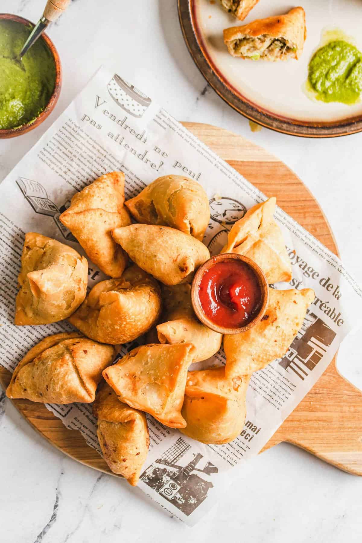 Samosas on sheet of newspaper set on wood cutting board