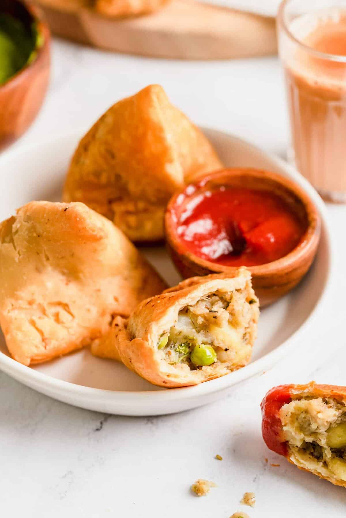 Samosas on plate with sauce, with one samosa cut open to show inside