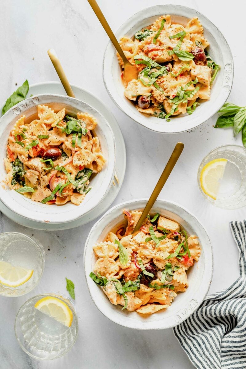 Three white bowls are filled with cheesy bowtie pasta.