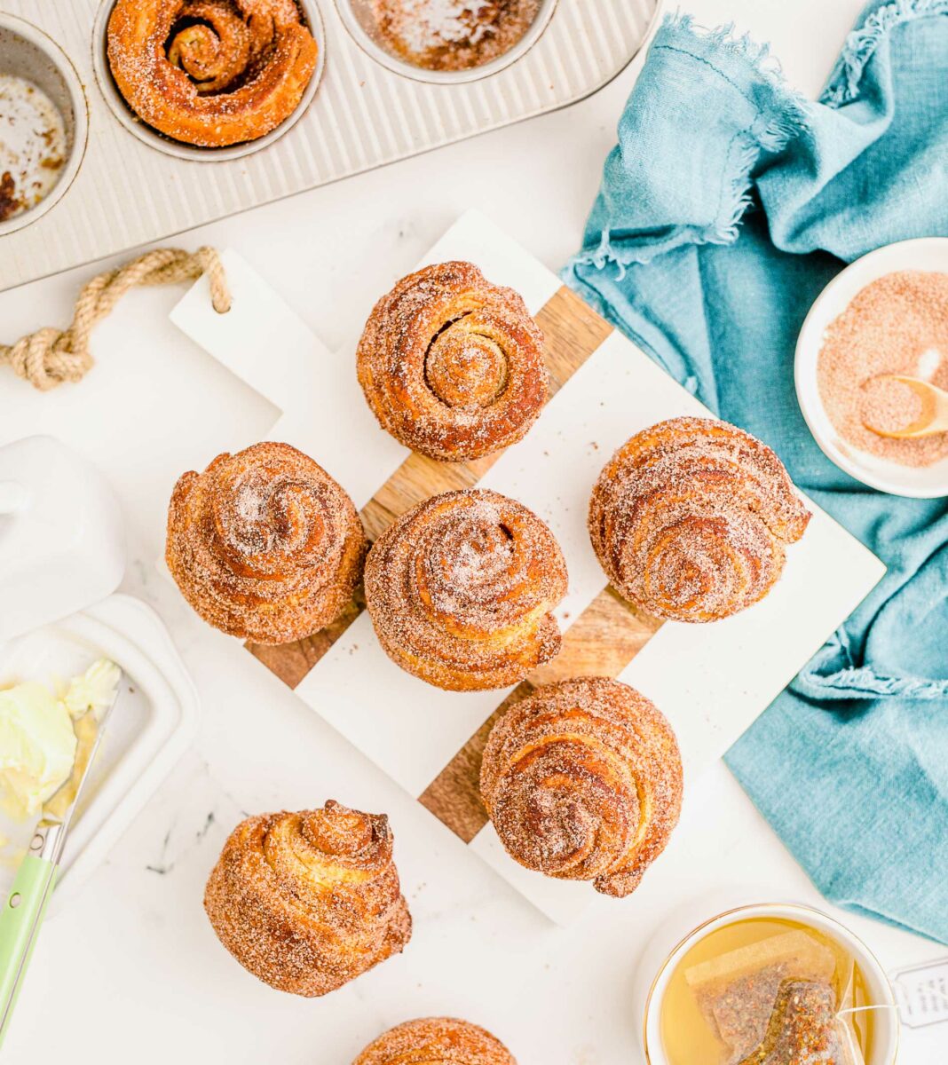 A batch of baked cruffins are spread out on a countertop next to various ingredients. 